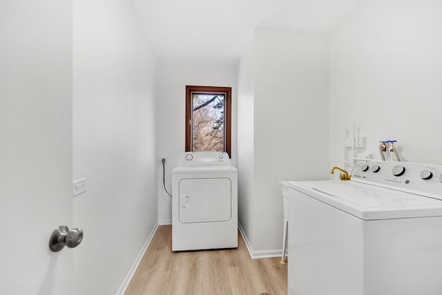 clothes washing area featuring washing machine and clothes dryer, laundry area, light wood-style flooring, and baseboards