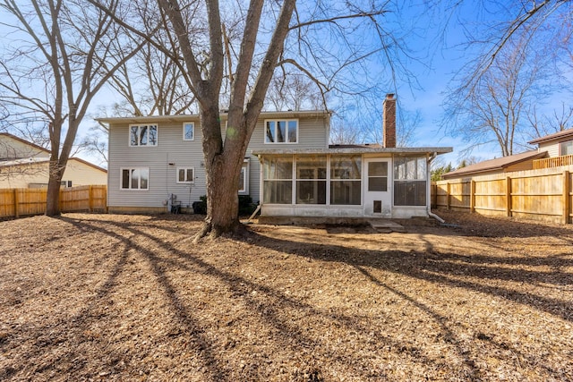 rear view of house featuring a fenced backyard, a chimney, and a sunroom