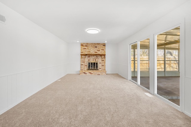 unfurnished living room featuring carpet flooring, a fireplace, and a wainscoted wall