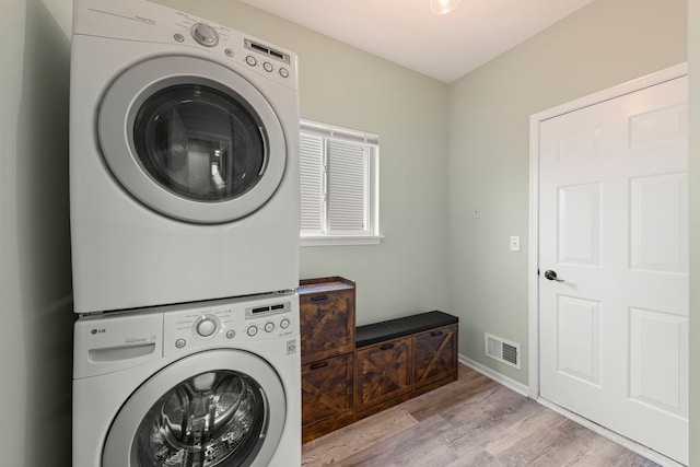 laundry room with laundry area, visible vents, baseboards, stacked washing maching and dryer, and light wood finished floors