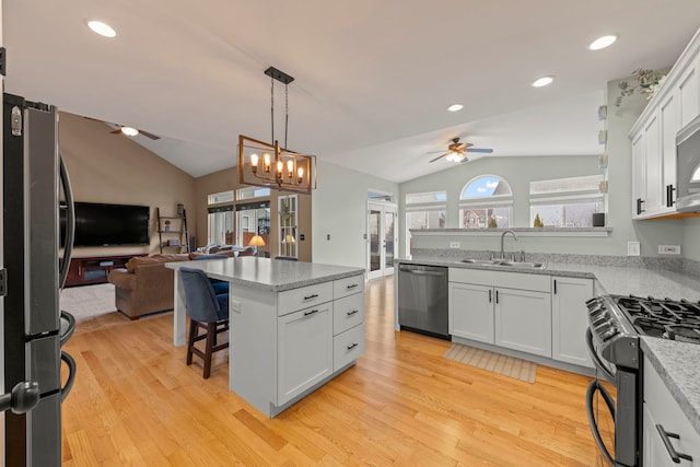 kitchen with appliances with stainless steel finishes, open floor plan, a sink, and vaulted ceiling