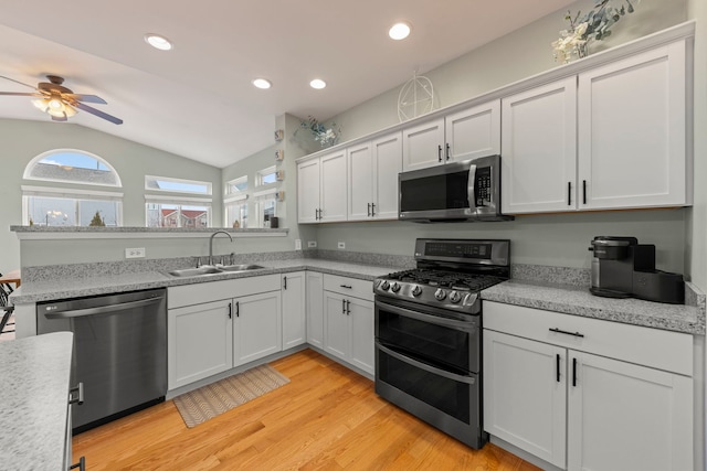 kitchen with stainless steel appliances, a sink, white cabinets, light wood-style floors, and light countertops