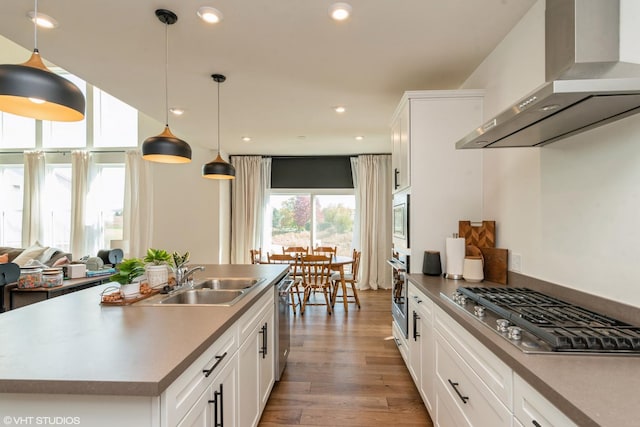 kitchen with a sink, white cabinetry, wood finished floors, wall chimney range hood, and appliances with stainless steel finishes