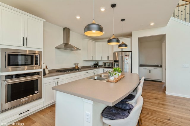 kitchen featuring a toaster, a sink, light wood-type flooring, wall chimney exhaust hood, and appliances with stainless steel finishes