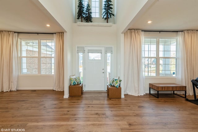 foyer entrance featuring baseboards, wood finished floors, a towering ceiling, and recessed lighting