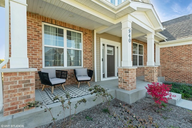 view of exterior entry with brick siding, a porch, and roof with shingles