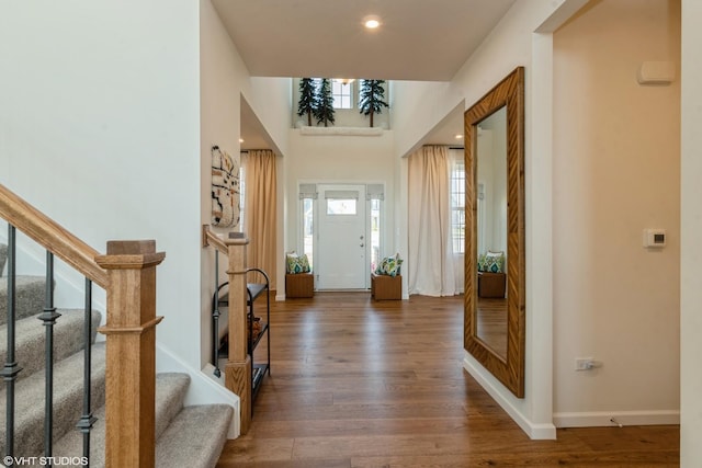 entrance foyer with stairs, a towering ceiling, baseboards, and wood finished floors