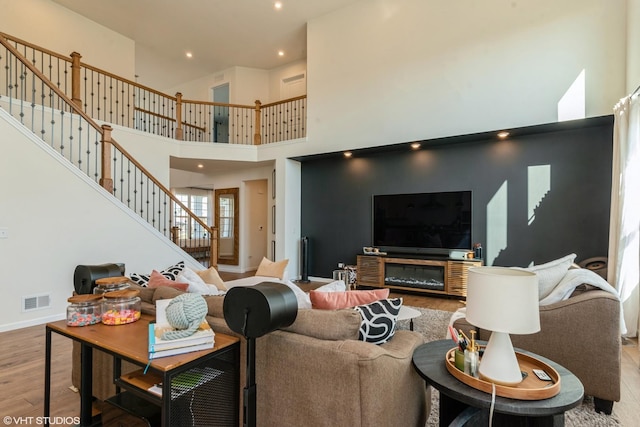 living area featuring baseboards, visible vents, a towering ceiling, wood finished floors, and stairs