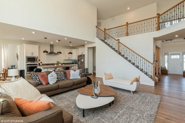 living area with a high ceiling, stairway, light wood-type flooring, and recessed lighting