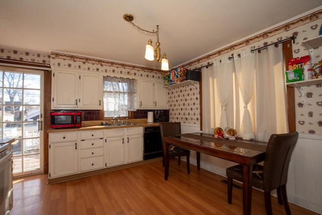 kitchen featuring a sink, white cabinetry, black dishwasher, light wood finished floors, and pendant lighting