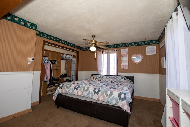 carpeted bedroom featuring a wainscoted wall, a textured ceiling, a ceiling fan, and wallpapered walls