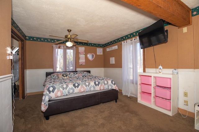 carpeted bedroom with wainscoting, a textured ceiling, multiple windows, and wallpapered walls