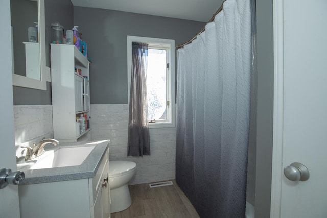 full bath featuring tile walls, visible vents, toilet, vanity, and wood finished floors