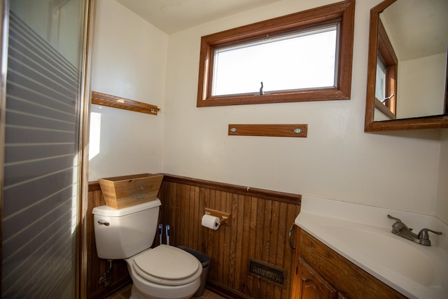 half bath featuring toilet, vanity, visible vents, and wainscoting