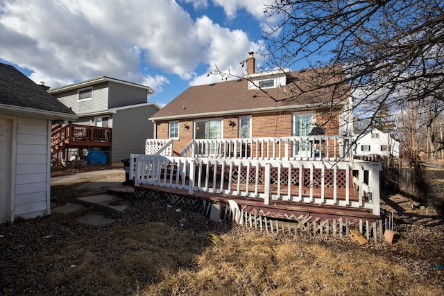 rear view of property featuring a shingled roof, brick siding, a chimney, and a wooden deck