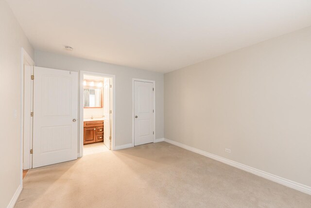 unfurnished bedroom with baseboards, light carpet, and ensuite bath