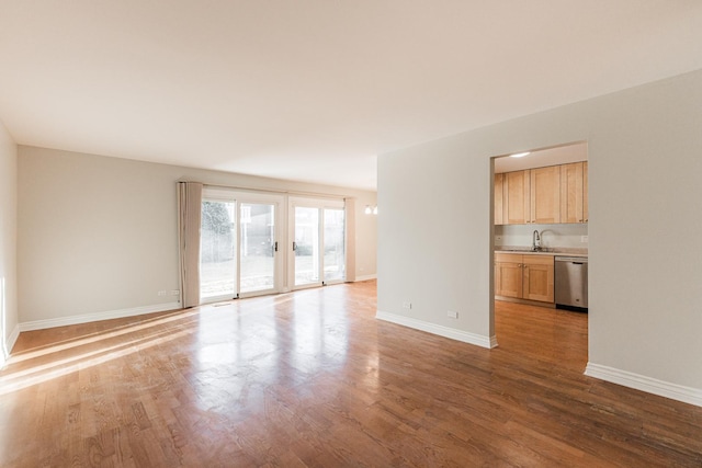 unfurnished living room featuring light wood-style floors, baseboards, and a sink