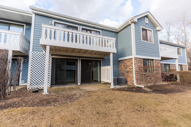 rear view of property featuring brick siding, central AC unit, and a balcony