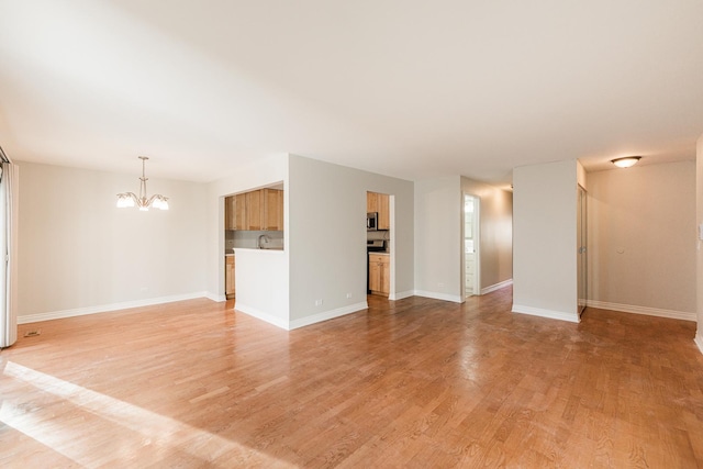 unfurnished living room with a notable chandelier, light wood-style flooring, and baseboards