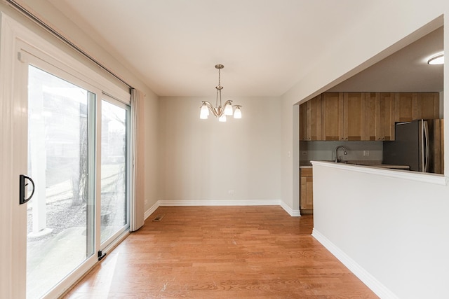 unfurnished dining area featuring a sink, a chandelier, baseboards, and light wood-style flooring