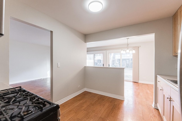 kitchen with gas stove, baseboards, light wood-style flooring, light countertops, and a notable chandelier