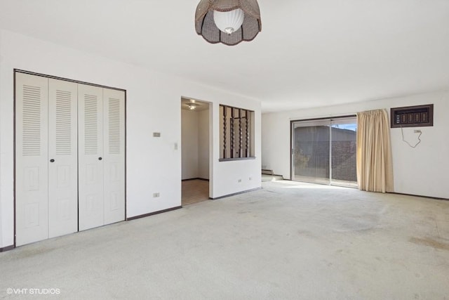 unfurnished bedroom with a closet, light carpet, an AC wall unit, and baseboards