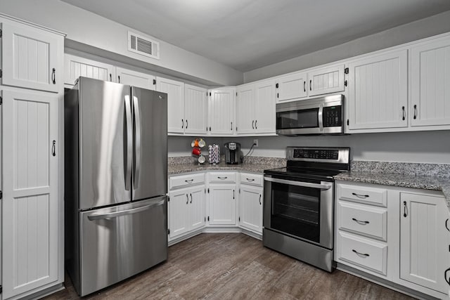kitchen featuring appliances with stainless steel finishes, dark wood-type flooring, white cabinetry, and light stone counters