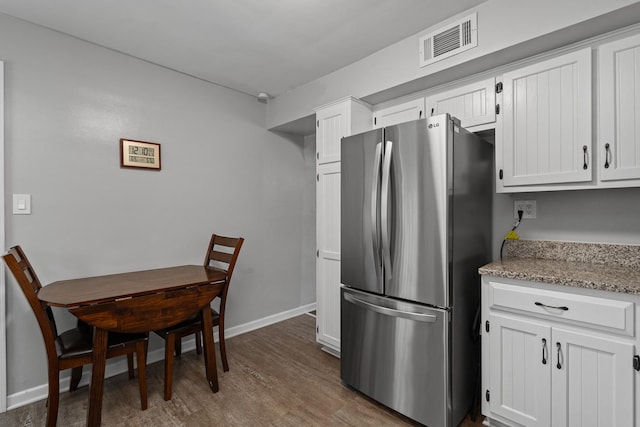 kitchen featuring freestanding refrigerator, baseboards, dark wood finished floors, white cabinetry, and light stone countertops