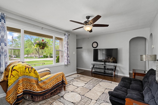 living area with ceiling fan, arched walkways, wood finished floors, and baseboards