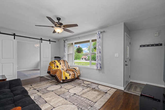 sitting room with ceiling fan, a barn door, wood finished floors, and baseboards