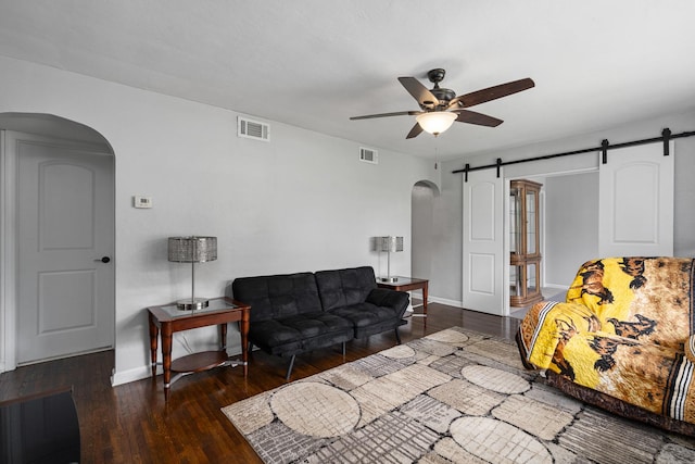 living room with arched walkways, ceiling fan, a barn door, baseboards, and wood finished floors