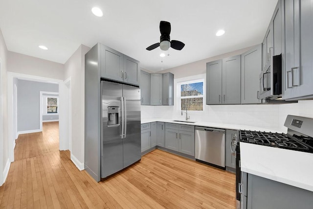 kitchen featuring light wood finished floors, stainless steel appliances, gray cabinets, decorative backsplash, and a sink