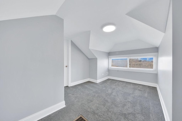 additional living space with vaulted ceiling, dark colored carpet, visible vents, and baseboards