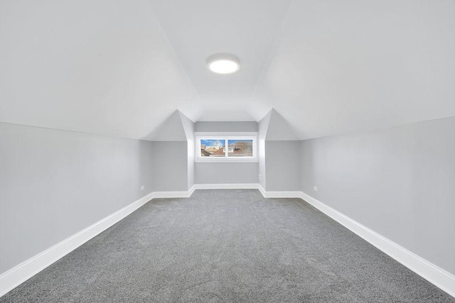 additional living space featuring dark colored carpet, lofted ceiling, and baseboards