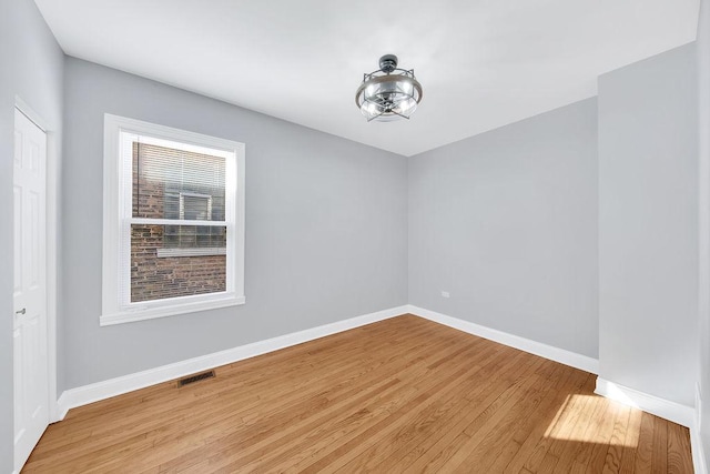 empty room with wood finished floors, visible vents, and baseboards