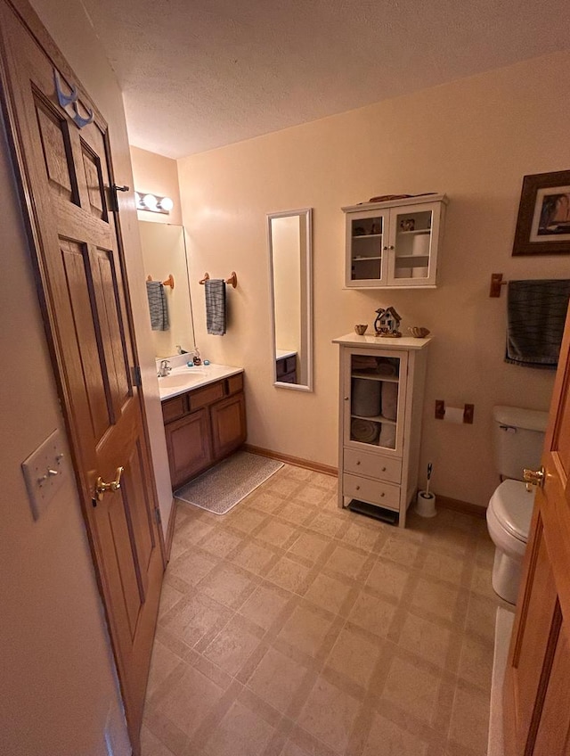 bathroom with a textured ceiling, toilet, vanity, baseboards, and tile patterned floors