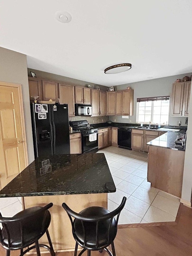 kitchen featuring a breakfast bar area, dark stone countertops, black appliances, a sink, and light tile patterned flooring