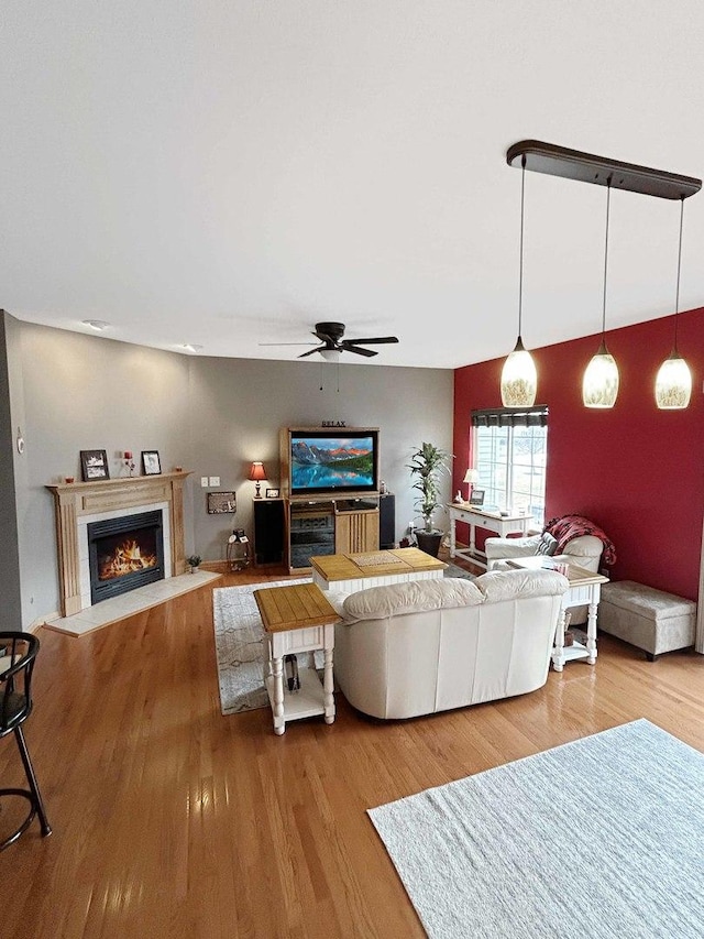 living area featuring a warm lit fireplace, ceiling fan, and wood finished floors