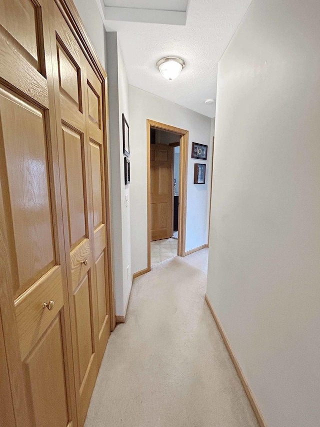 hallway with light carpet, baseboards, and a textured ceiling