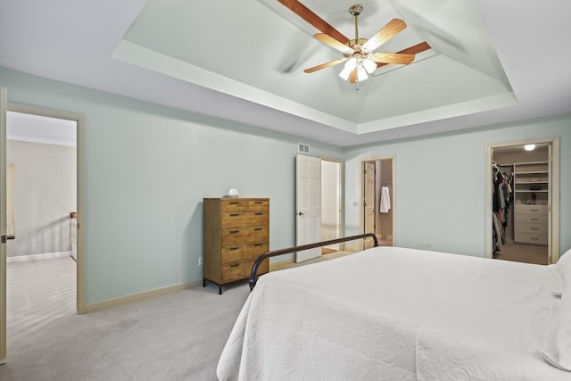 bedroom with a walk in closet, a raised ceiling, light colored carpet, visible vents, and baseboards