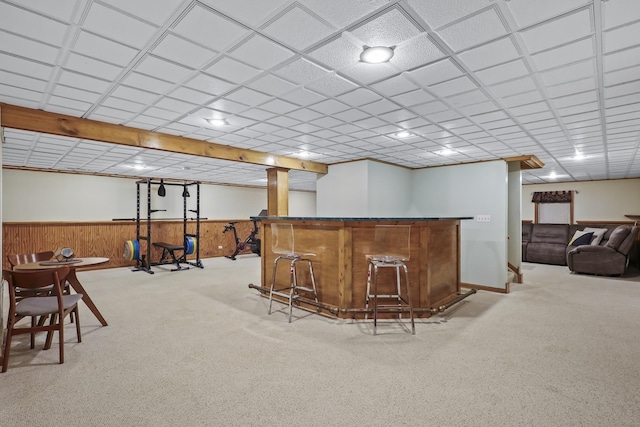 bar featuring a drop ceiling, wainscoting, carpet flooring, a bar, and wood walls