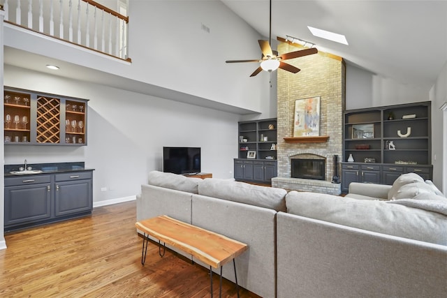 living area with visible vents, light wood-style flooring, a brick fireplace, wet bar, and baseboards