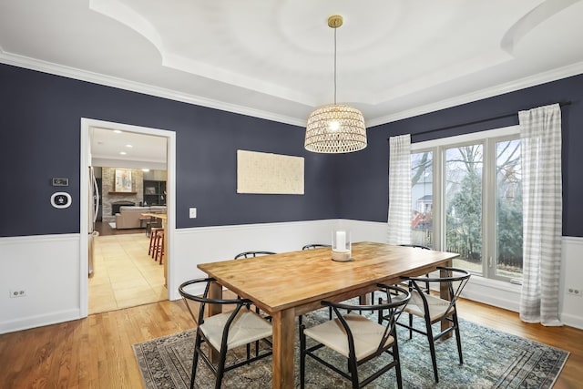 dining room with light wood-style floors, a tray ceiling, a wainscoted wall, and crown molding