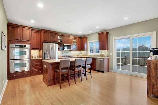 kitchen featuring a breakfast bar, stainless steel appliances, glass insert cabinets, light wood-type flooring, and a center island