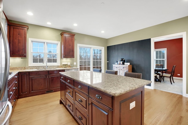 kitchen featuring light stone counters, a center island, light wood-type flooring, and a sink