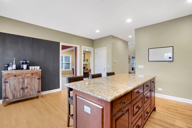 kitchen with light wood-type flooring, a kitchen bar, baseboards, and light stone countertops