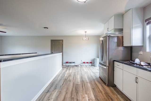 kitchen featuring light wood finished floors, baseboards, white cabinets, dark countertops, and freestanding refrigerator