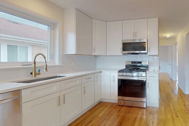 kitchen with light wood finished floors, white cabinetry, appliances with stainless steel finishes, and a sink