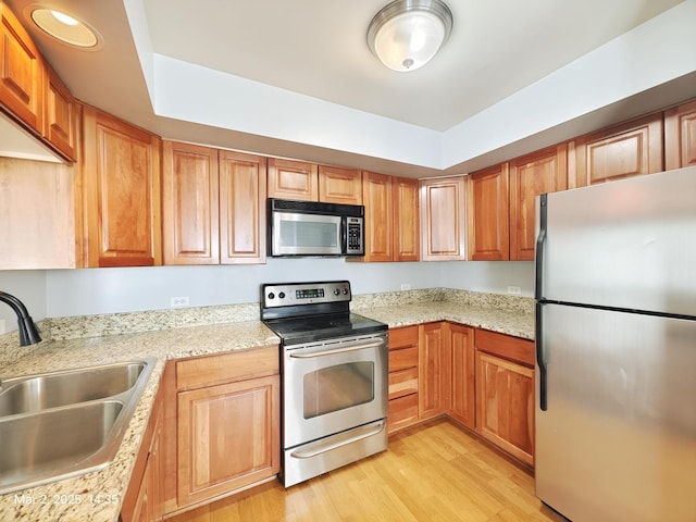 kitchen featuring light stone counters, stainless steel appliances, a sink, brown cabinets, and light wood finished floors