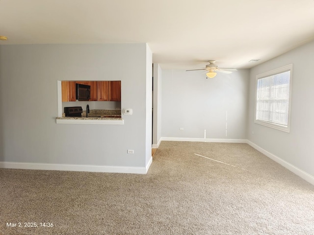 unfurnished living room featuring a ceiling fan, light colored carpet, a sink, and baseboards